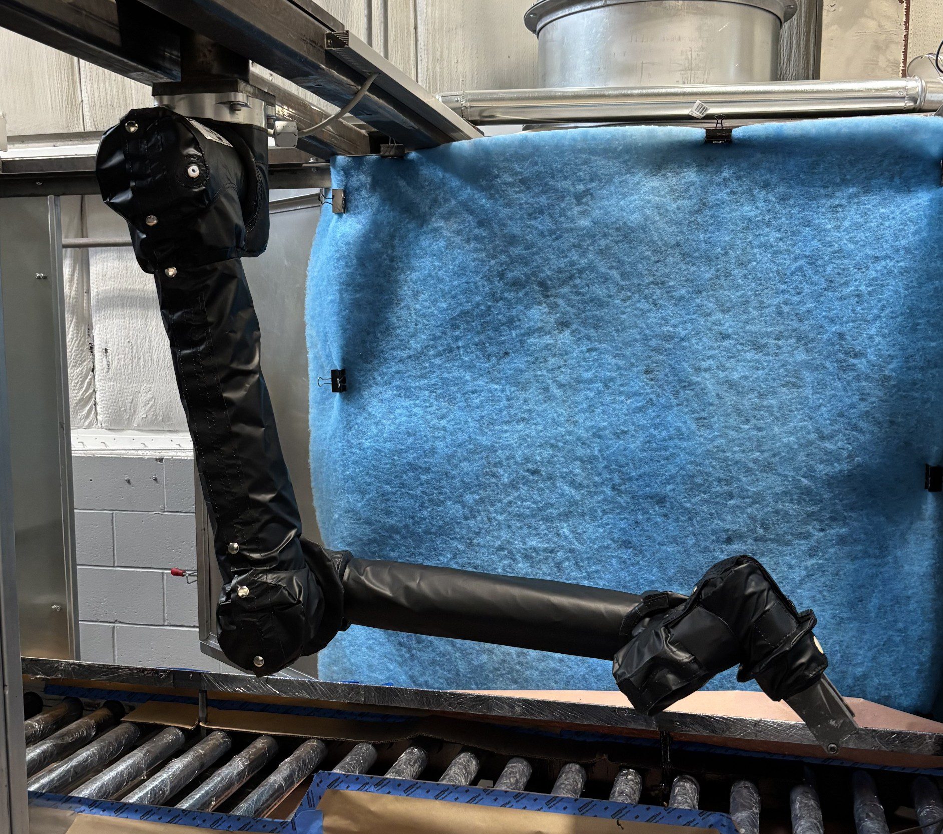 Robotic arms handling a blue fabric piece on a conveyor belt.