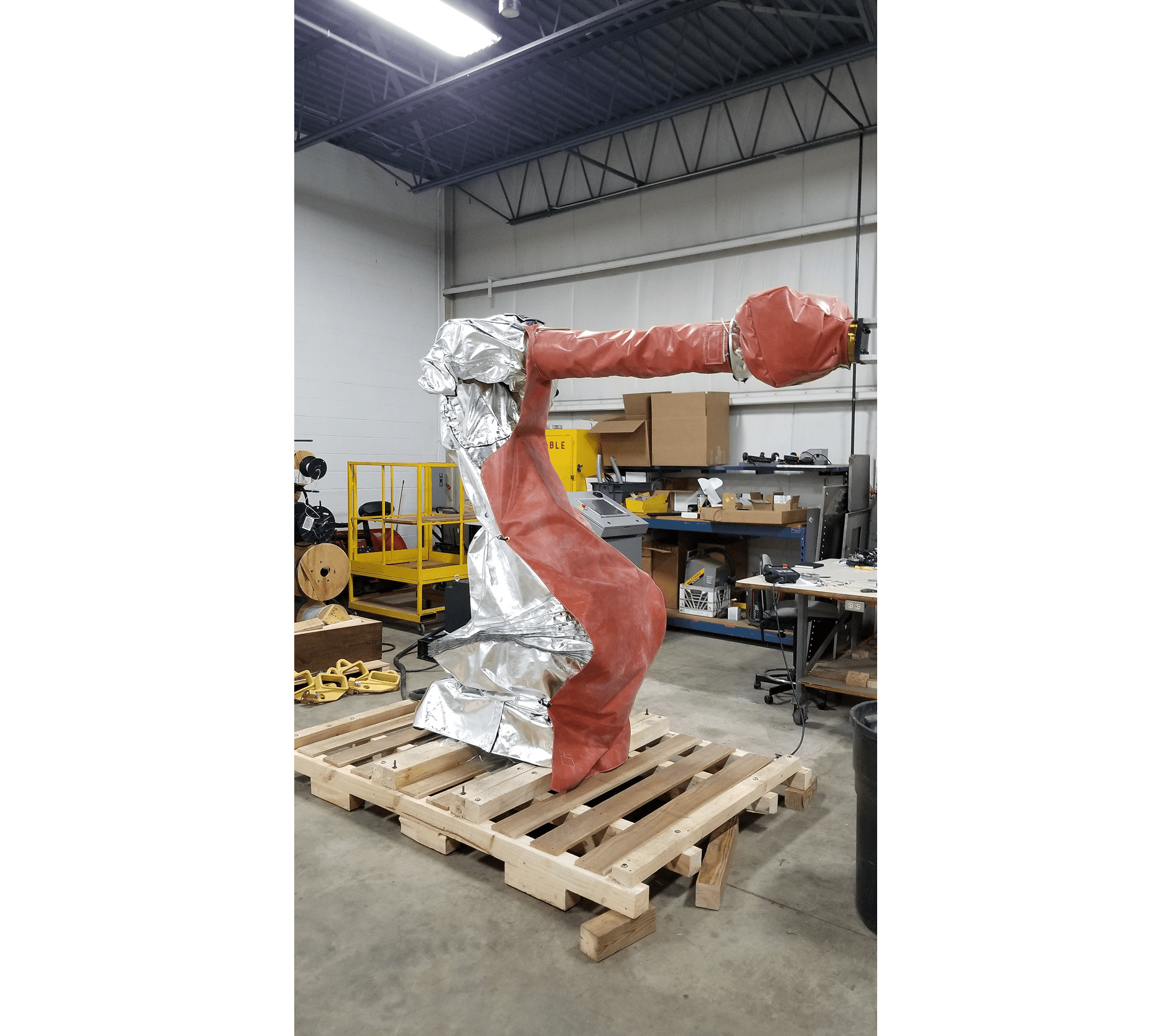 Industrial robotic arm on a wooden pallet in a workshop.