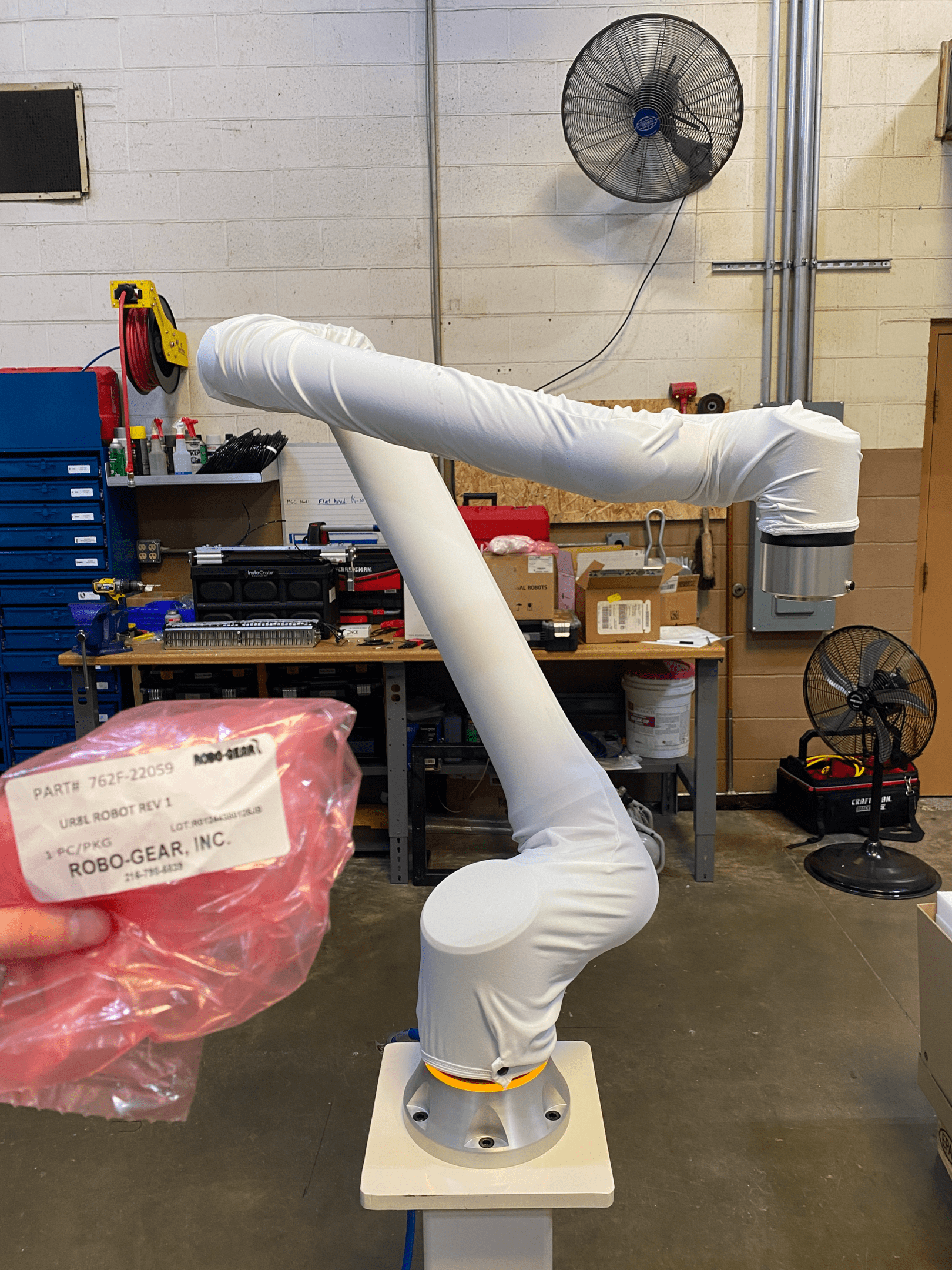 Robot arm wrapped in white protective material inside a workshop.